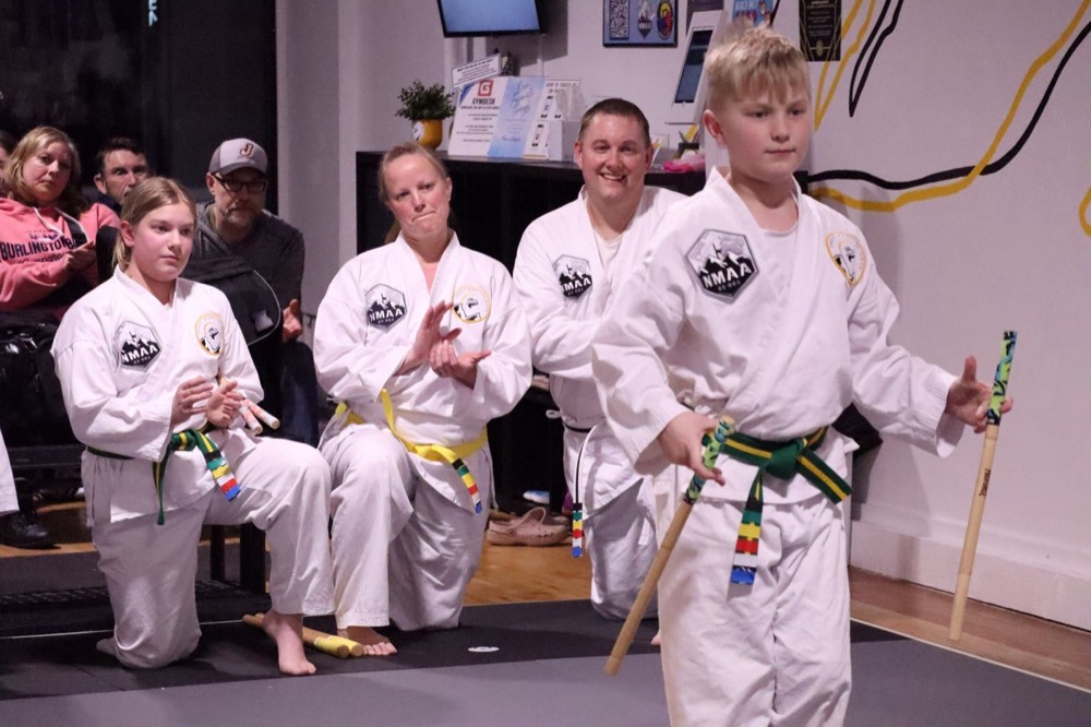 Parents and kids in uniform cheering a student through his weapons form